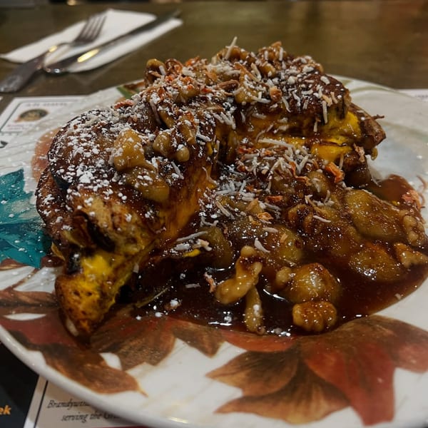 French toast topped with bananas, walnuts, powdered sugar, and shredded coconut on a decorative plate.